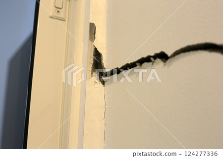 Close-up of a large crack running vertically and horizontally across an interior wall. 124277336