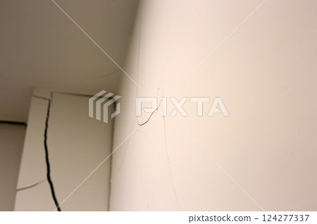 Close-up of a large crack running vertically and horizontally across an interior wall. 124277337