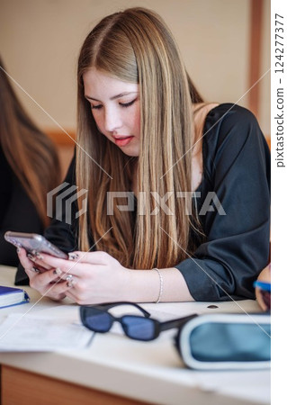 High school student using mobile phone in classroom while studying, with virtual reality headset and sunglasses on desk High school student using mobile phone in classroom while studying, with virtual reality headset and sunglasses on desk 124277377
