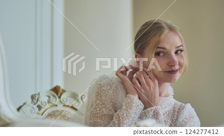Beautiful young bride wearing elegant wedding dress putting on earrings, preparing for her wedding ceremony Beautiful young bride wearing elegant wedding dress putting on earrings, preparing for her wedding ceremony 124277412