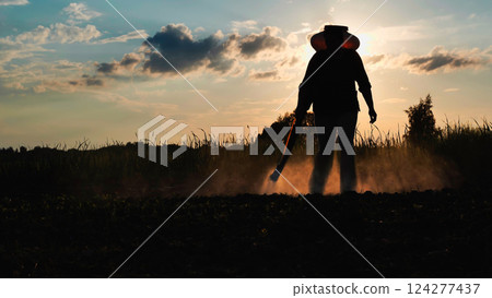 Farmer silhouetted while spraying pesticide over agricultural field, blocking insect damage during golden evening light 124277437