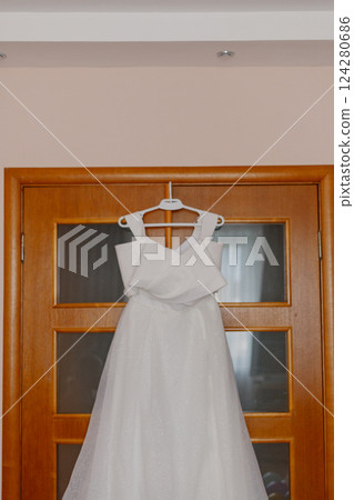A beautiful white wedding dress hangs on a wooden A beautiful white wedding dress hangs on a wooden 124280686
