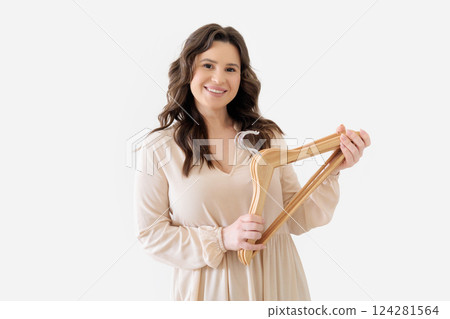 Young beautiful girl in beige dress holds several empty wooden clothes hangers Young beautiful girl in beige dress holds several empty wooden clothes hangers 124281564