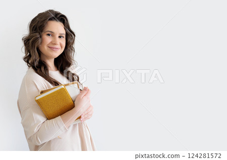 Beautiful European woman in beige suit holds stack of gold and white diaries. White background.  124281572