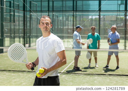 Portrait of sporty male padel player with a racket and ball in his hands on the background of tennis court 124281789