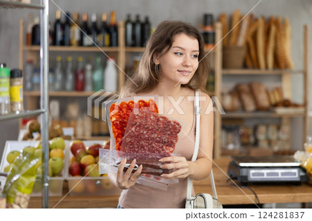 Girl pondering over choice of cured sausages in grocery shop 124281837