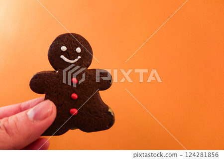 close up of finger holding a gingerbread biscuits in an orange background wall for Christmas close up of finger holding a gingerbread biscuits in an orange background wall for Christmas 124281856