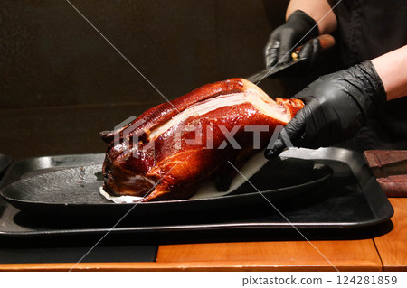 Close up of the chef wearing black gloves cutting and slicing the grilled Peking duck Close up of the chef wearing black gloves cutting and slicing the grilled Peking duck 124281859