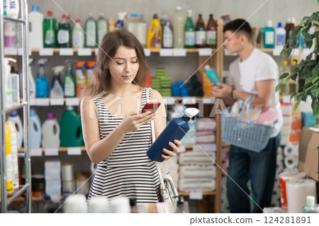Girl buyer scans qr code on tile cleaner spay label, man shopping in background Girl buyer scans qr code on tile cleaner spay label, man shopping in background 124281891