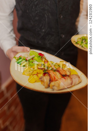 The waiter holds a plate of food in his hands in a 124281960