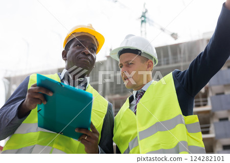 Young civil engineer discussing a construction plan with a colleague shows him something 124282101