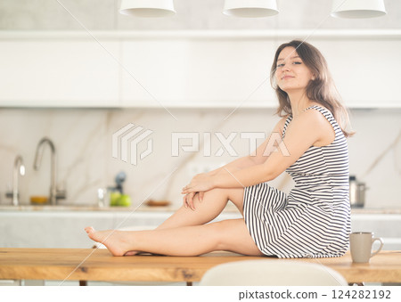 Young woman sitting on table in kitchen Young woman sitting on table in kitchen 124282192
