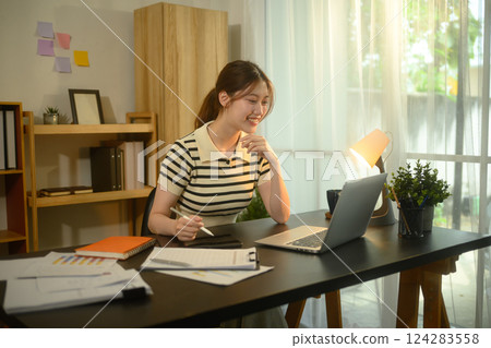 Smiling woman working in a bright home office with laptop and documents Smiling woman working in a bright home office with laptop and documents 124283558