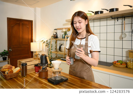 Young woman in apron preparing pour over coffee in a cozy home kitchen Young woman in apron preparing pour over coffee in a cozy home kitchen 124283576