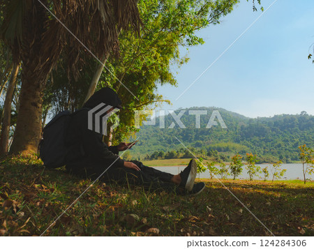 solo traveler man sit and relax under tropical tree with lake background 124284306