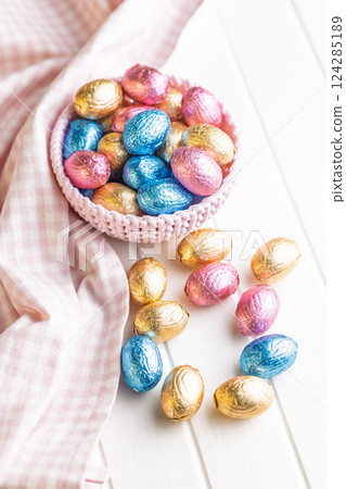 Chocolate easter eggs wrapped in multi colored foil in bowl on white table. 124285189