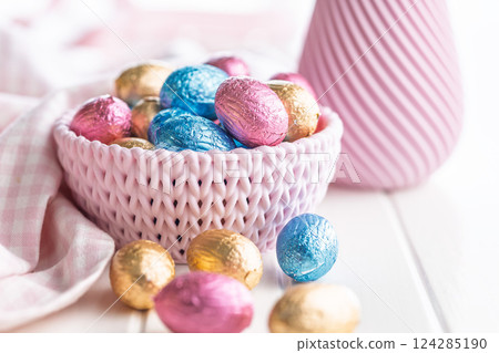Chocolate easter eggs wrapped in multi colored foil in bowl on white table. Chocolate easter eggs wrapped in multi colored foil in bowl on white table. 124285190
