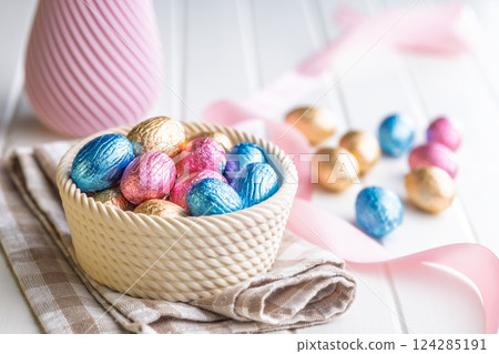 Chocolate easter eggs wrapped in multi colored foil in bowl on white table. Chocolate easter eggs wrapped in multi colored foil in bowl on white table. 124285191