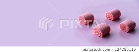 Four pink cupcakes resembling rolled pastries are arranged on a soft rose-patterned surface. 124286119