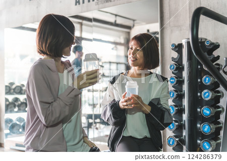 一名女子和她的朋友在健身房休息，飲用蛋白質和 EAA 飲料 124286379
