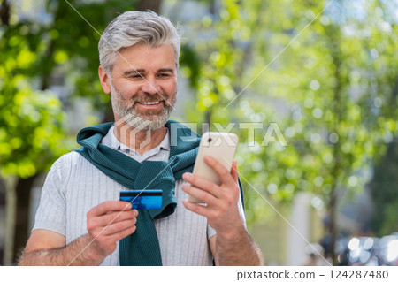Happy mature man use credit bank card smartphone while transferring money purchases online shopping 124287480