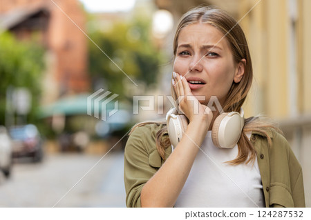 Portrait of young Caucasian woman traveler standing outdoors feeling toothache on city street Portrait of young Caucasian woman traveler standing outdoors feeling toothache on city street 124287532