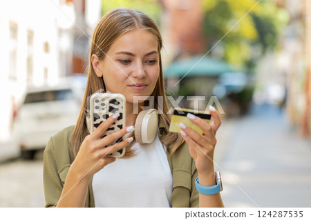 Caucasian woman using credit card and smartphone while transferring money, purchases online outdoors Caucasian woman using credit card and smartphone while transferring money, purchases online outdoors 124287535