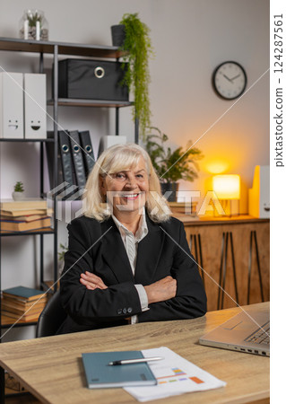Smiling senior businesswoman using laptop computer and looking at camera at home office table Smiling senior businesswoman using laptop computer and looking at camera at home office table 124287561