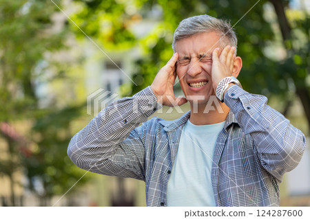 Displeased man rubbing temples to cure headache problem suffering from migraine stress on street 124287600