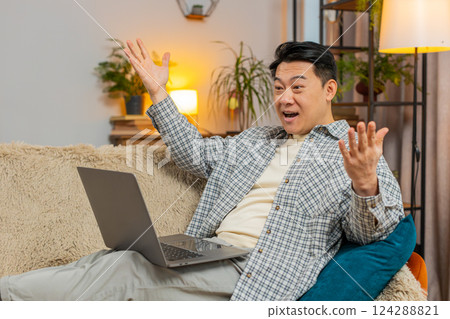 Excited man sitting on sofa using laptop receives good news victory celebrate lottery win at home Excited man sitting on sofa using laptop receives good news victory celebrate lottery win at home 124288821