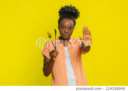African American woman holding fork and knife, finger no gesture, refusing food, diet control, focus African American woman holding fork and knife, finger no gesture, refusing food, diet control, focus 124288848