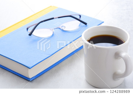 Image of a book, glasses and a coffee mug on a white table, enjoying reading while drinking coffee 124288989
