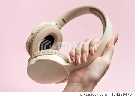Woman holding wireless headphones on pink background 124289479