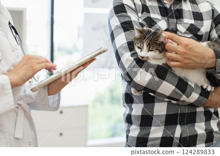 Veterinarian using tablet to explain medical history or prescription to man holding cat. Image shows assistance, animal care, and interaction with advanced technology 124289833