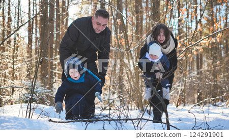 Family enjoying winter landscape, walking together through snow covered forest, sharing warmth and happiness on sunlit day 124291901