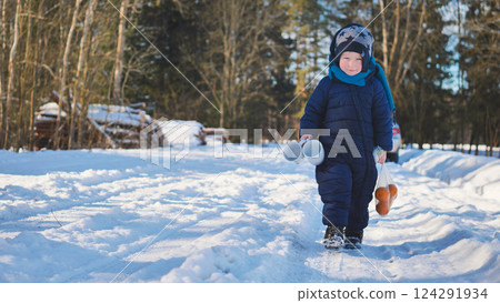 Happy child wearing winter clothes carrying mugs and food walking on snowy road in a winter forest Happy child wearing winter clothes carrying mugs and food walking on snowy road in a winter forest 124291934