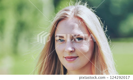 Portrait of a beautiful blonde woman with blue eyes and freckles smiling serenely in a natural outdoor setting 124292017