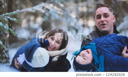 Winter forest scene with happy parents hugging children, radiating love and warmth amid falling snowflakes 124292026