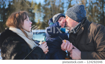 Parents sharing citrus fruit with smiling toddler during bright winter outdoor playtime 124292046