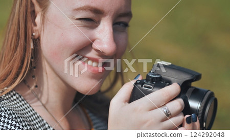 Professional camera balanced in hands, female photographer winking playfully during outdoor shoot, expressing creative joy 124292048