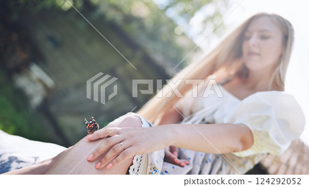 Young blonde woman gently touching a butterfly landed on her leg, enjoying a sunny summer day outdoors 124292052
