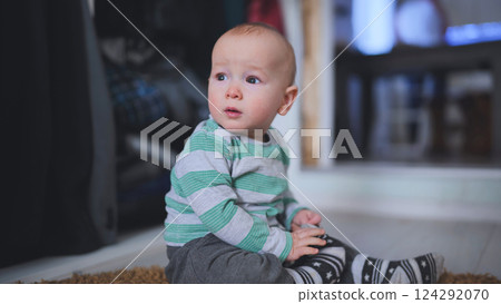 Infant sitting barefoot, exploring tiny toes while gazing sideways, capturing pure childhood wonder in soft, warm indoor environment Infant sitting barefoot, exploring tiny toes while gazing sideways, capturing pure childhood wonder in soft, warm indoor environment 124292070