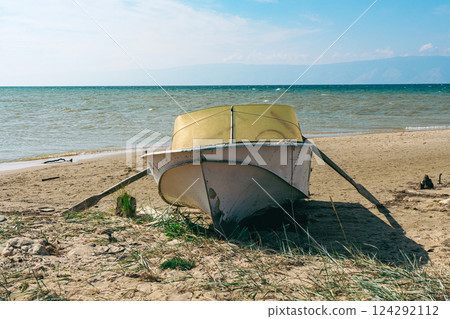 Old fishing boat stands on sand, lake shore 124292112