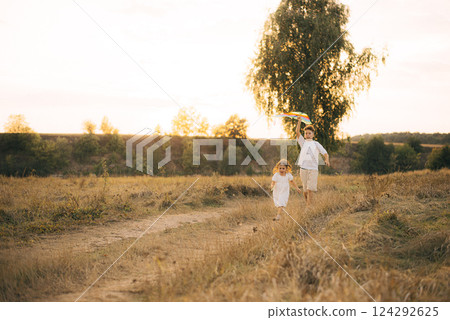 Older brother and sister running with a kite Older brother and sister running with a kite 124292625