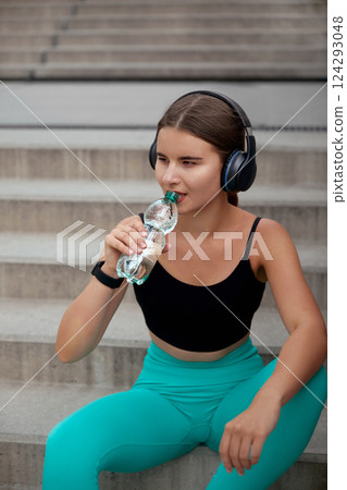 Women Enjoying Fitness Break While Sitting on Stairs and Drinking Water in Activewear Outdoors Women Enjoying Fitness Break While Sitting on Stairs and Drinking Water in Activewear Outdoors 124293048
