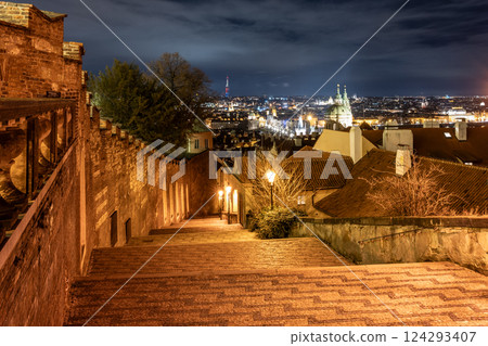 Under the moonlight, the Prague Castle staircase reveals a stunning view of the city's illuminated skyline. The warm light creates a captivating ambiance, inviting evening strolls. 124293407