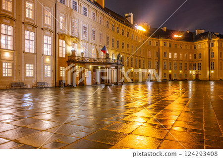 At dusk, the entrance door of Prague Castle features a balcony overlooking the Third Courtyard, with reflections on the wet stone pavement creating a serene atmosphere. 124293408