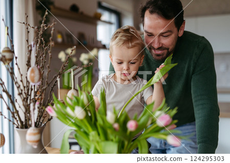 Father and little son arranging tulips in a vase. 124295303
