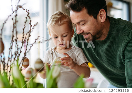 Father and little son decorating pussy willows branches, putting easter eggs on them. Father and little son decorating pussy willows branches, putting easter eggs on them. 124295316