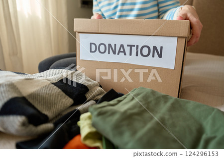 Woman holding donation box with clothes on bed 124296153